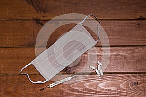 Face mask with a mercury clinical thermometer and tablets on a brown wood background.