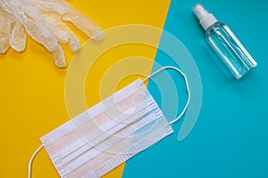 Face mask, plastic and transparent gloves and antiseptic gel on a blue and yellow background