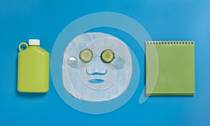 Face mask , reusable nwater bottle, cucumber, notepad on blue background. Dehydration.