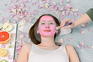 Face mask, skin care, spa procedures. Beautiful young girl at spa, lying on bed with flower petals and fresh fruits