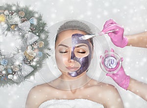 Face mask the skin to beautiful woman. Next to her are Christmas decorations.New Year`s and Cosmetology concept