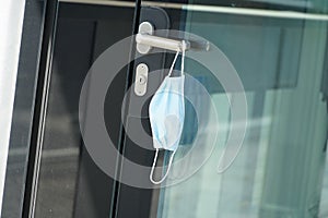 A face mask suspended on a door handle in a corporate building, close up. A reminder of safety measures in prevention of coronavir