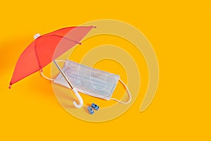 face mask under a red umbrella on yellow background, beach vacation and tourism during the coronavirus epidemic concept