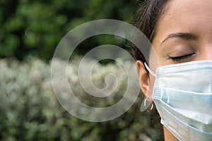 Face of a mask-wearing woman with her eyes closed in outdoor background