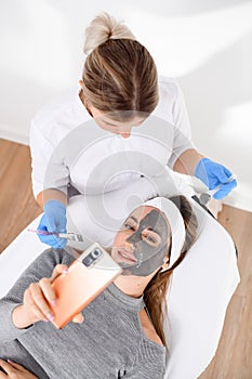 Face mask for a woman in a gray sweater with a mobile in hand, lying on a salon couch