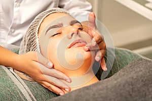 Face massage. Beautiful caucasian young white woman having a facial massage with closed eyes in a spa salon.