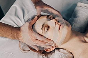 Face massage. Male hands make head massage to a beautiful young woman. Close-up of a woman getting spa treatment