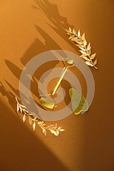 Face massage roller and gua sha with dried leaves on beige background. Facial skin care concept