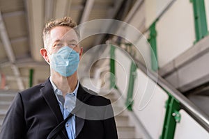 Face of mature businessman with mask going down the stairs of the sky train station