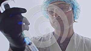 The face of a medic who fills a syringe from a bottle with blue liquid The face of a man in a protective mask and hands