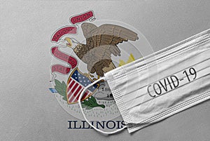 Face Medical Surgical White Mask with COVID-19 inscription lying on Illinois State Flag. Coronavirus in Illinois