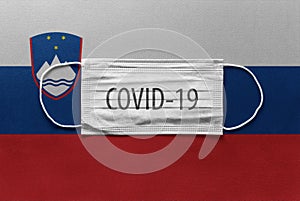 Face Medical Surgical White Mask with COVID-19 inscription lying on Slovenia National Flag. Coronavirus in Slovenia