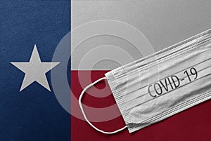 Face Medical Surgical White Mask with COVID-19 inscription lying on Texas State Flag. Coronavirus in Texas