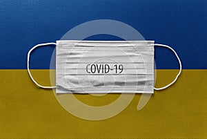 Face Medical Surgical White Mask with COVID-19 inscription lying on Ukraine National Flag. Coronavirus in Ukraine