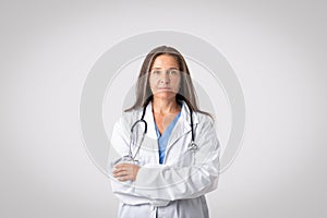 The face of modern healthcare. Portrait of confident senior doctor woman posing with folded arms, light background