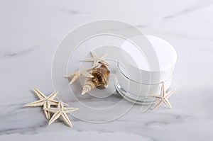 Face moisturizer, shell and starfishes on the white marble surface