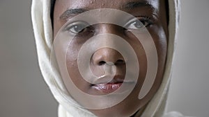 Face ofoung sad african muslim girl in hijab is looks up and watching at camera, religioun concept, grey background