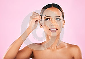 Face, pain and woman with tweezer for eyebrow in studio isolated on a pink background. Beauty, facial plucking and hair