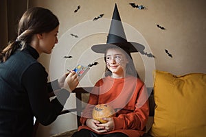 face paints for halloween. woman draws web for child with brush.