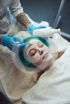 Face peeling mask, spa beauty treatment, skincare. Woman getting facial care by beautician at beauty salon.