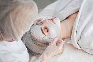 Face peeling mask, spa beauty treatment. Woman getting facial care by beautician at spa salon.