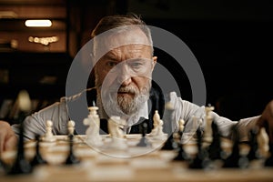 Face portrait of confident senior man looking at chess pieces