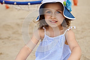 Face portrait of a cute beautiful little girl wearing sunhat and relaxing on the sand background. Summer camp