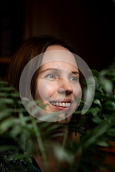 Face portrait of a middle aged woman in green plants smiling. A woman in her forties. Relaxation, calm state, happy face