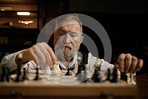 Face portrait of senior man moving chess piece on board during competition match