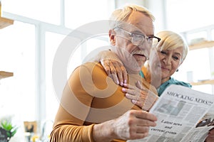 Face portrait of spouse reading paper while wife cuddling him