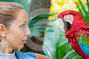Face portrait of young girl looking at red macaw parrot