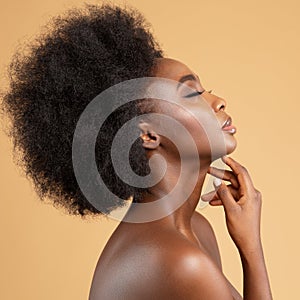 Face Profile of African Beauty Woman massaging Face and Neck. Dark Skin Model with Afro Hairstyle Side view over Beige