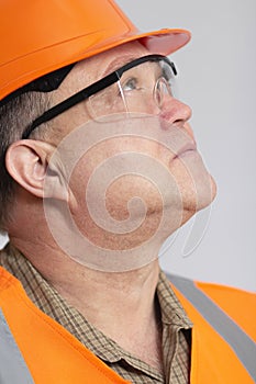 Face profile of thoughtful plump engineer in protective glasses, construction worker in hard hat onstudio background