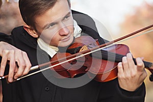 Face profile of a young elegant man playing the violin on autumn nature backgroung, a boy with a bowed orchestra instrument makes