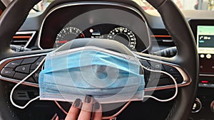 A face protection mask in female fingers on a steering wheel