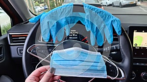 A face protection mask in female hand against a car steering wheel