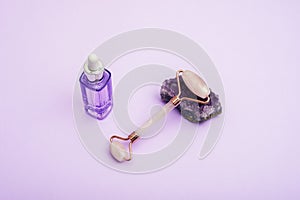 Face roller on amethyst crystal and purple serum bottle. Moisturizer and skincare tools. Spa and wellness concept. Top