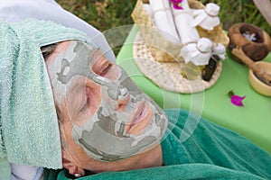 The face of senior woman is covered by facial clay mask