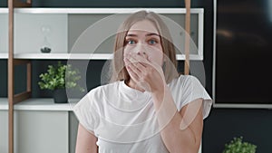 Face of shocked terrified young woman. A frightened young female with wide open eyes covers her mouth with her hand