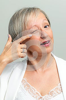 Face shot of middle age woman pointing with finger at crow`s feet on face