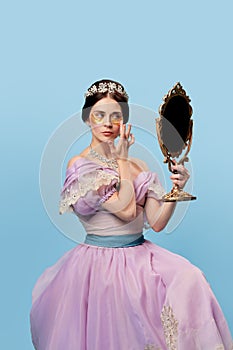 Face skin care. Beautiful charming woman in lilac color vintage dress as a royal person, princess looking in mirror at