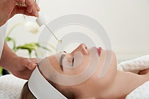 Face Skin Care. Closeup Of Beautiful Smiling Woman Receiving Serum Oil Treatment In Beauty Salon. Cosmetologist Applying