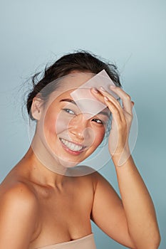 Face skin care. Smiling woman using oil blotting paper portrait