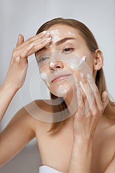 Face skin care. Woman applying facial cleanser on face closeup