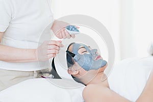 Face Skin Care. Woman doing facial procedures to beautician. The spa staff is applying mud to the face