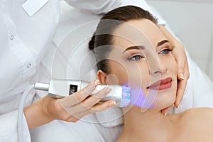 Face Skin Cosmetology. Closeup Woman Doing Blue Light Treatment