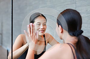 Face of smiling young asian woman looking at her reflection in mirror to camera