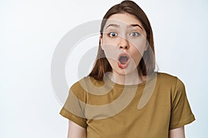 Face of surprised beautiful girl, saying wow, looking impressed at camera with oval-shaped mouth, standing in awe