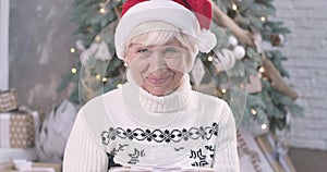 Face of surprised mature Caucasian woman holding Christmas gift box, looking at camera and smiling. Pleasant lady