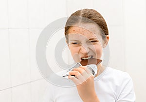 Face of a teenage girl with pimples, acne on the skin, she looks at herself in the mirror and eating a chocolate, concept of